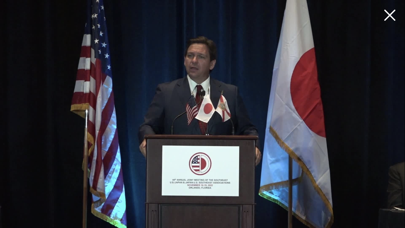 Ron DeSantis wearing a suit and tie in front of a curtain